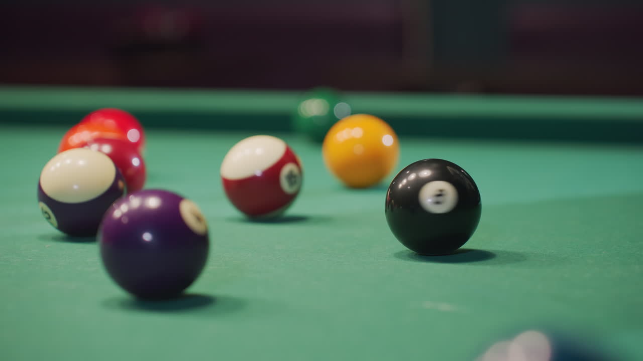 Close-up of hand rolling black billiard ball on green pool table, surrounded by vibrant colorful balls. Focus on motion, precision, and dynamics of gameplay as ball moves across smooth felt surface