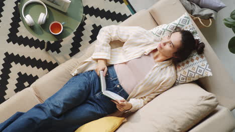 young woman resting on sofa and reading book