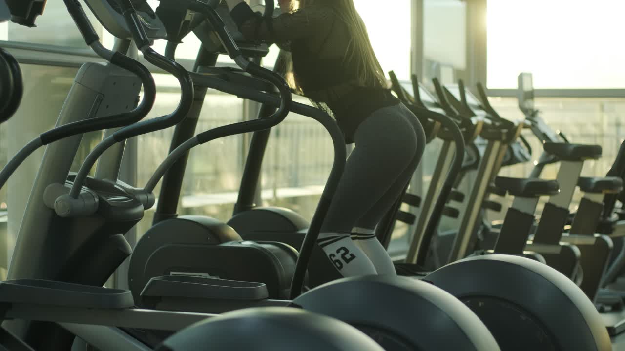 Una donna atleta cammina sull'ellittica in palestra. Una ragazza si allena sullo stepper per migliorare l'intensità cardiovascolare e la resistenza.