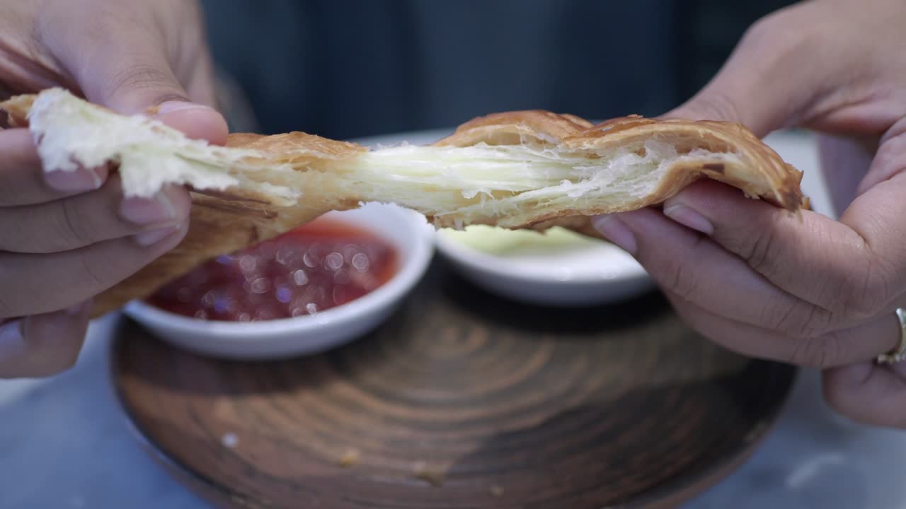 A person holding a croissant with butter and jam