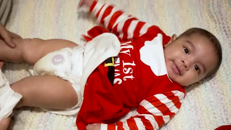 overhead view of cute 3 month old baby wearing red my 1st christmas outfit laid on blanket getting a nappy change