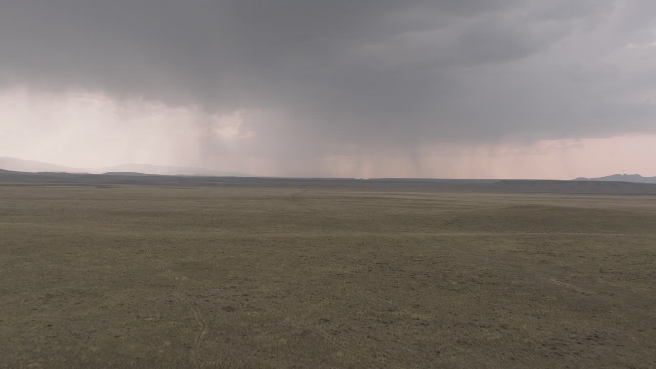 A vast stormy plain under a cloudy sky with rain falling in the distance
