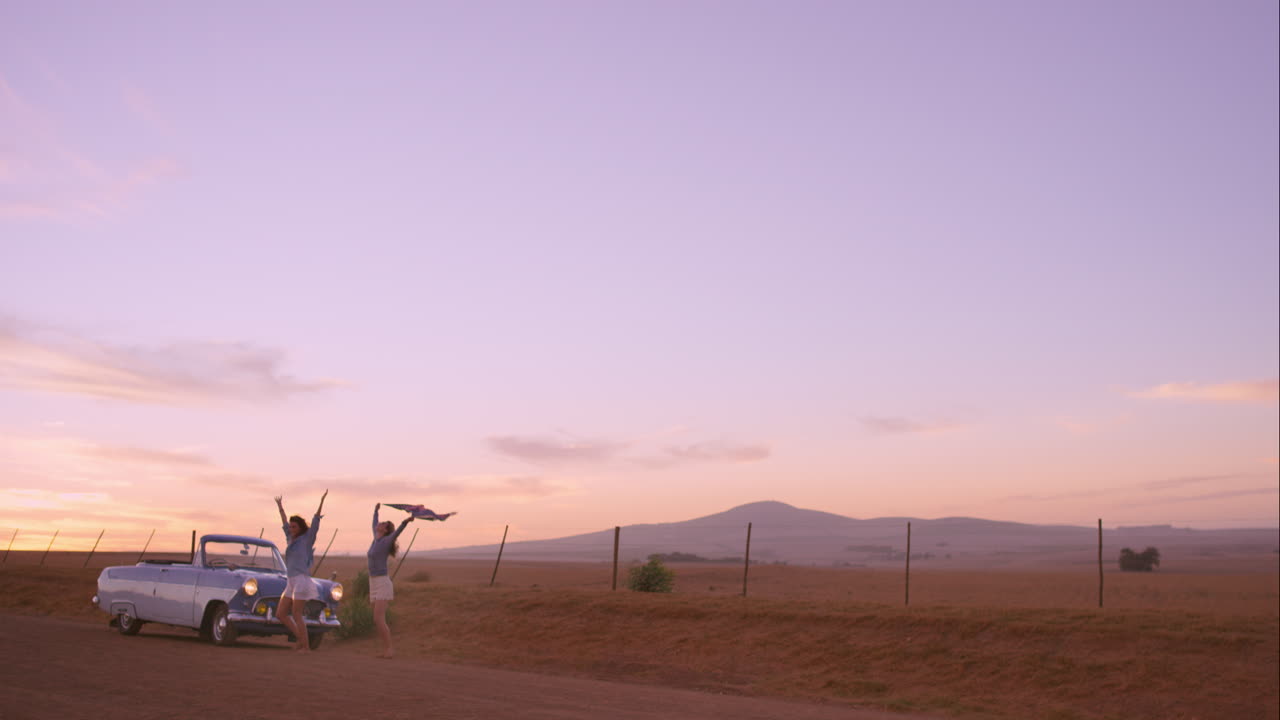 옛날 자동차 를 타고 도로 여행 에서 일몰 에 춤 을 추는 여자 친구 들
