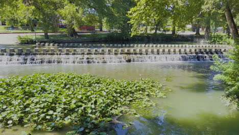 a small waterfall at a city park with beautiful trees on a sunny afternoon