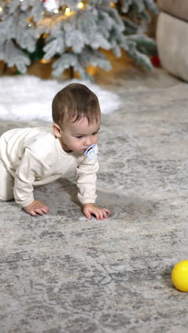 crawling caucasian toddler plays with balls on the floor. black domestic cat runs near baby. christmas tree at backdrop. vertical video