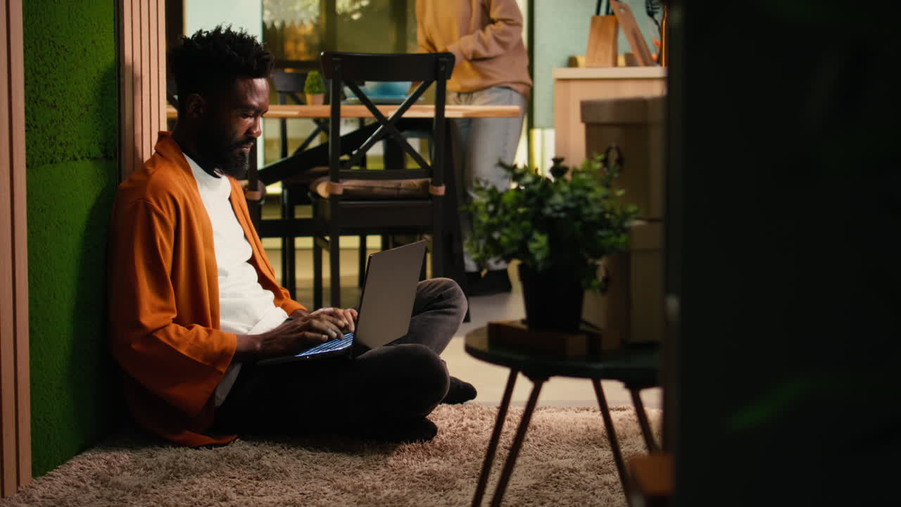 Cozy lifestyle scene of African American man relaxing indoors with his laptop