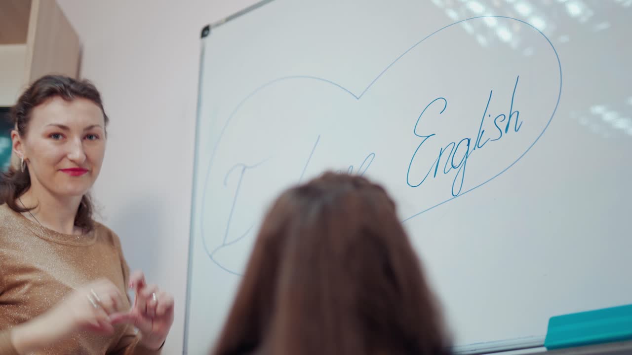 Teacher and little girl at school. Young teacher helps the pupil near the board. Female pedagogue draws the heart on a whiteboard. Back to school.