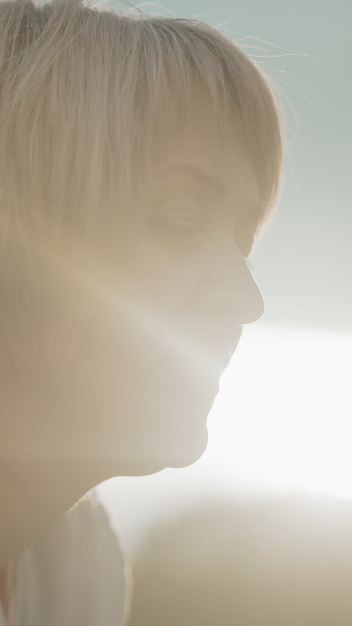 중년 여성이 집중된 표정으로 누워있고, 부드러운 황금빛에 둘러싸여 있으며, 구름이 가득한 하늘과 멀리 있는 나무는 평화롭고 반사적인 야외 환경을 만니다.