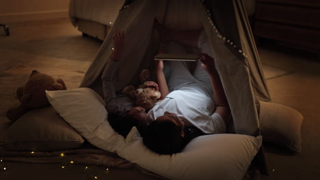 mother and daughter reading on tablet in a play tent