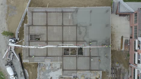 top view of construction men at work pouring and spreading concrete mix on slab floor of a building with installed rebars