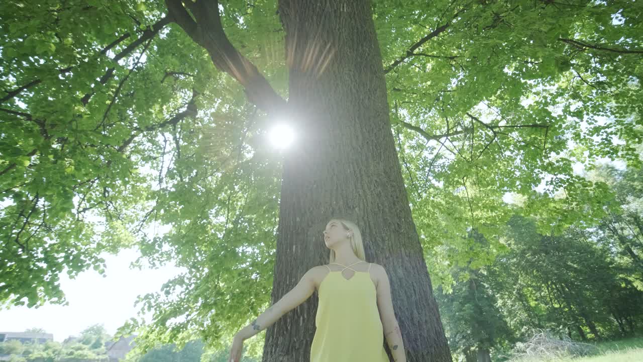 mujer con vestido amarillo bailando junto al árbol en el parque de verano