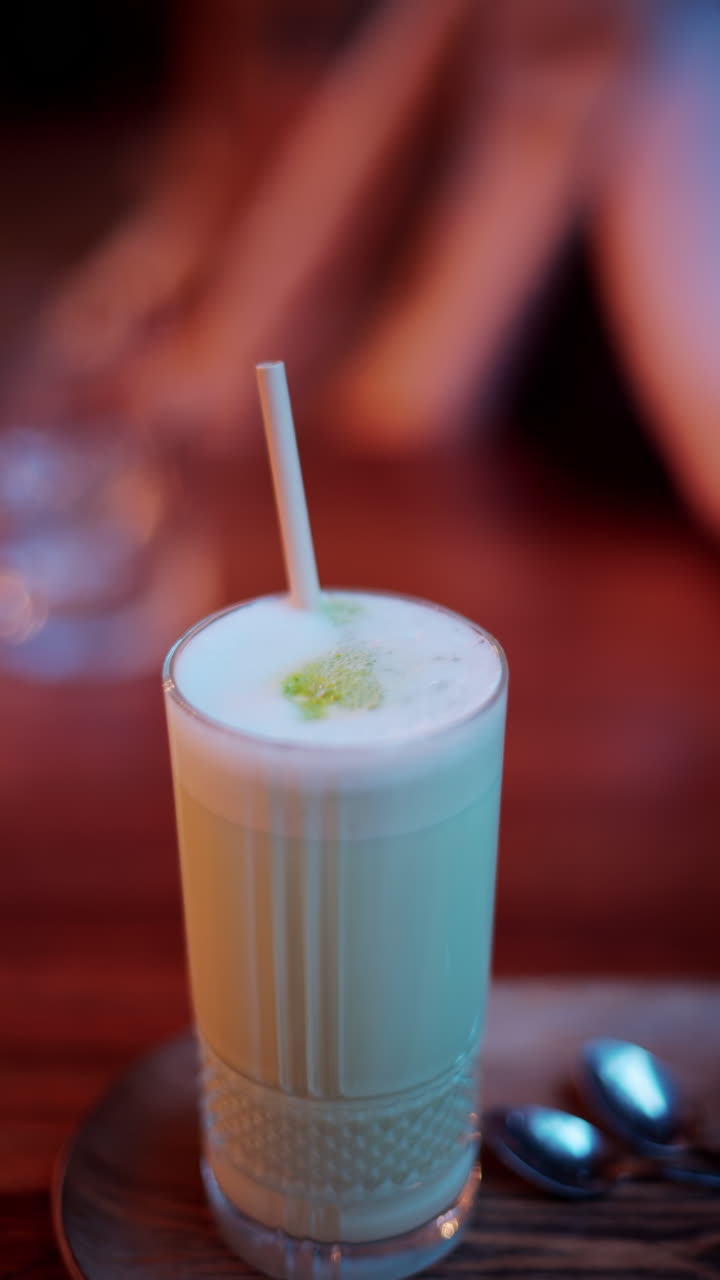 Bir kafede masanın üzerinde pipetli bir bardakta matcha latte yakın çekim. Dikey
