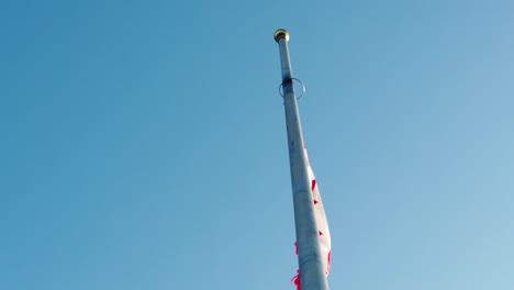 slow motion clip of red and white canadian flag blowing in the wind filmed from the side and back. bright blue sky on summer day. outdoors. mid shot