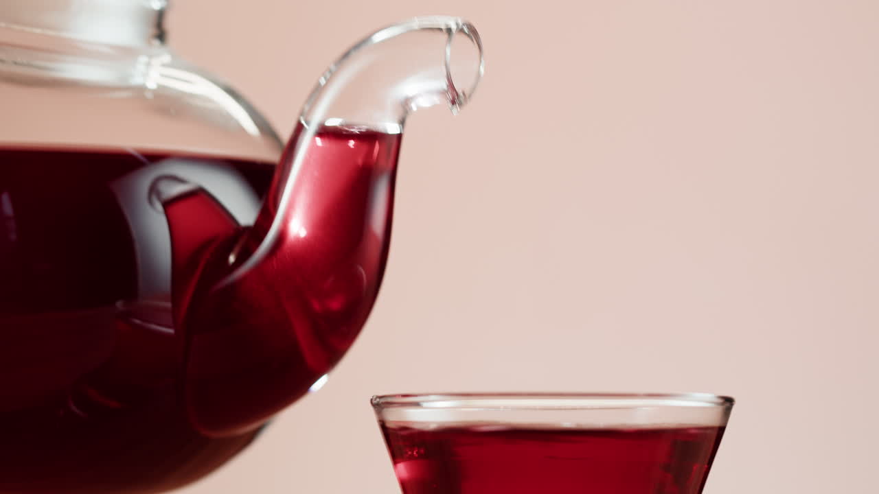 Red liquid being poured from a glass teapot into a cup