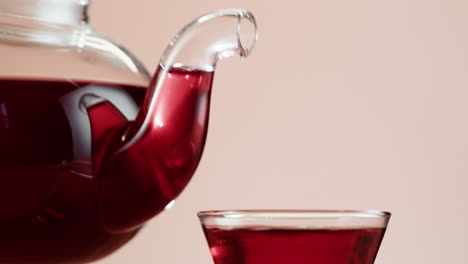 red liquid being poured from a glass teapot into a cup