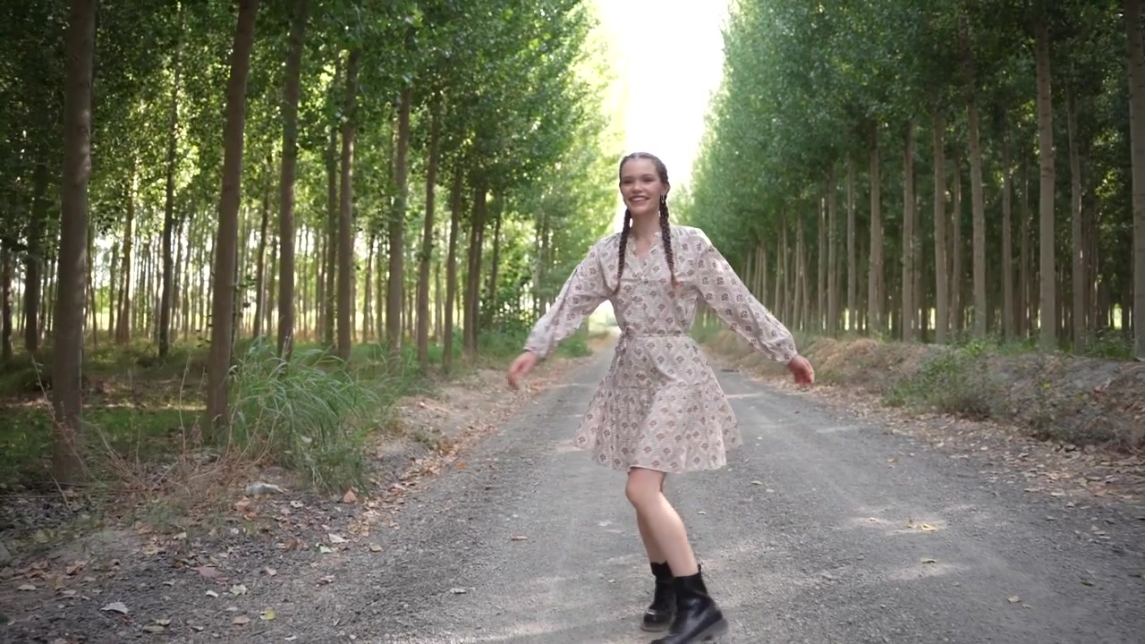 Una giovane donna volteggia gioiosamente in un abito floreale su un sereno sentiero di campagna, incarnando la felicità.