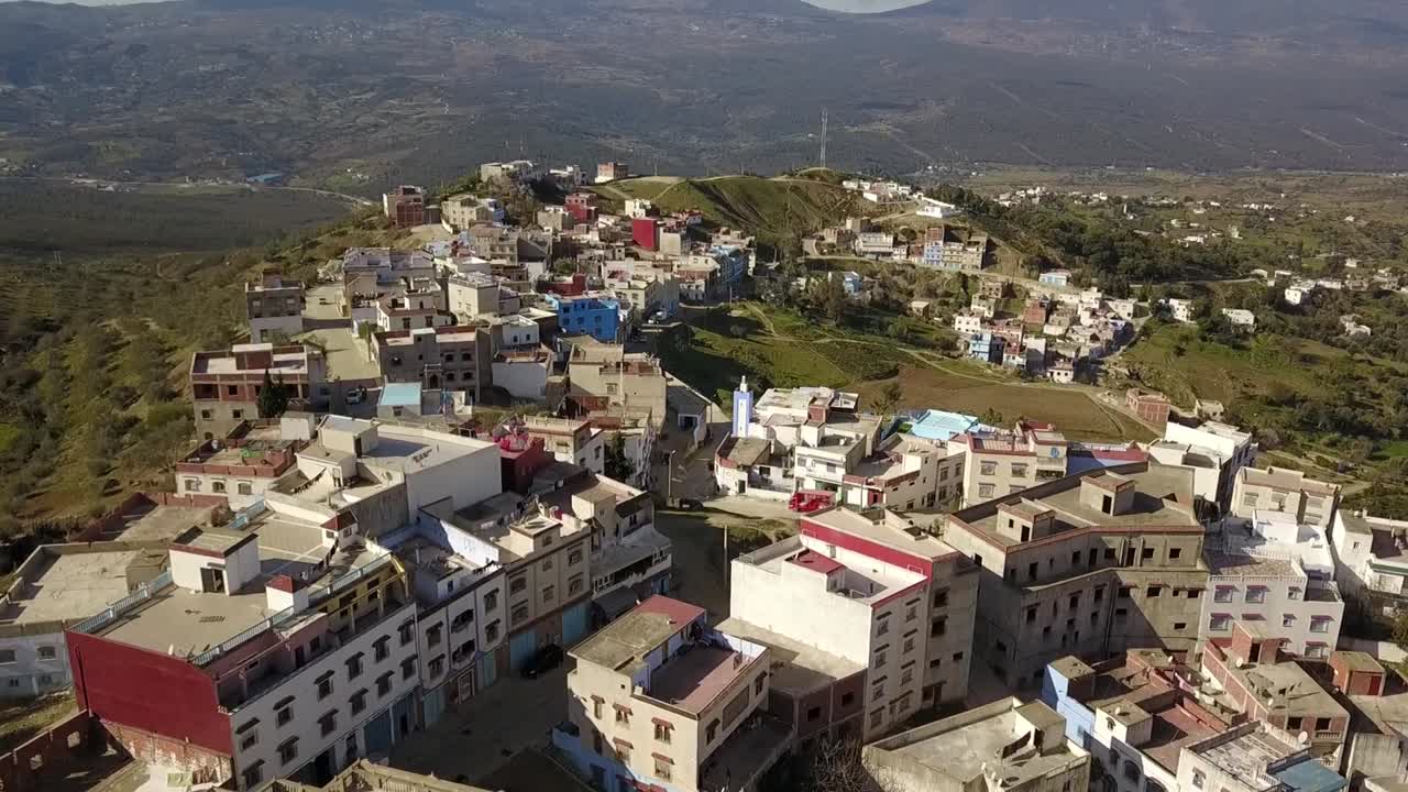 Veduta aerea di Chefchaouen, Marocco, che mostra case residenziali su un pendio con il paesaggio dei Monti del Rif e lo scenario urbano della città di giorno.