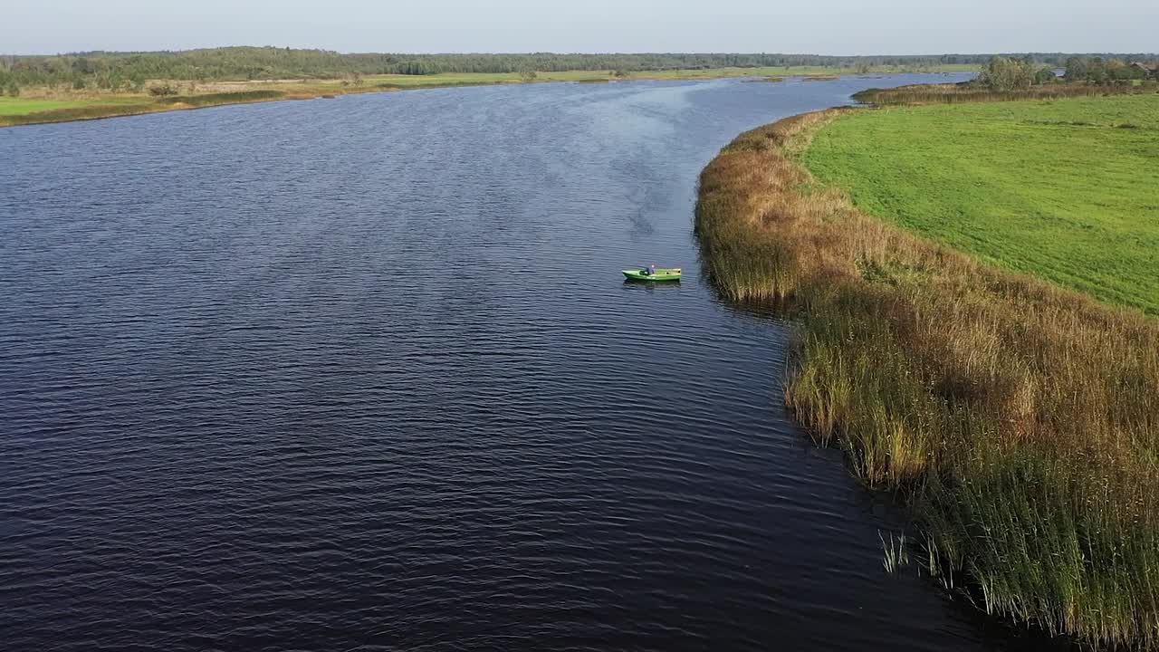 Moving towards shot with man on fishing boat who are fishing in the river near reeds
