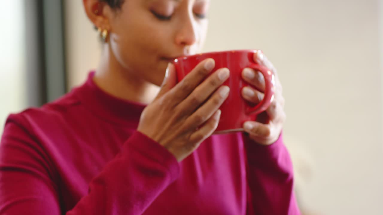 Donna di mezza età che nota una tazza rossa sul bancone di un bar, la solleva, ne inspira l'aroma e ne assaggia il contenuto