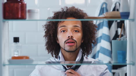 View-Through-Bathroom-Cabinet-Of-Young-Man-Putting-On-Tie-Before-Going-To-Work