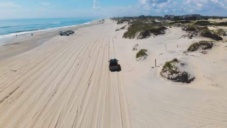 drone siguiendo suv negro en las orillas exteriores de la playa corolla 4x4