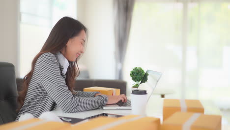 一位漂亮的亚洲女人在她的办公桌上工作, 周围是送货包裹,