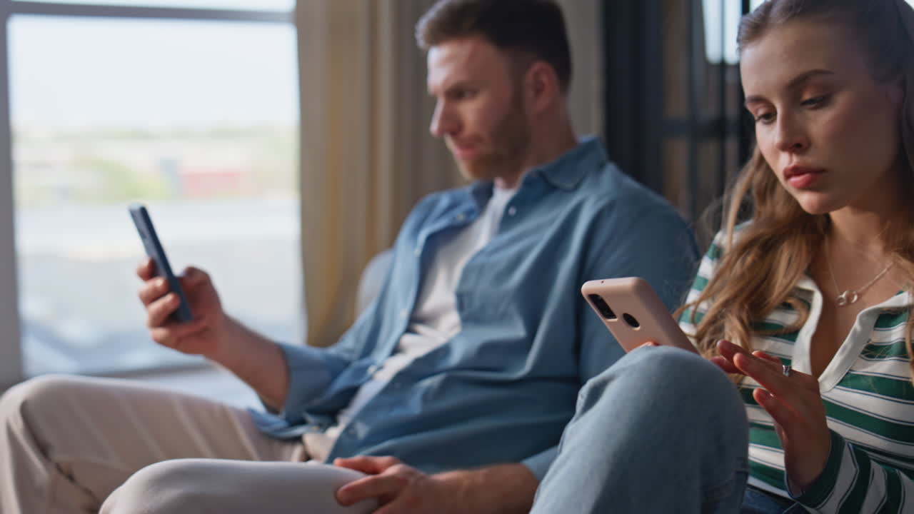 Closeup man finger scrolling smartphone at couch. Couple ignoring each other