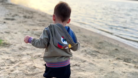 adorable smiling baby boy running by the shore. happy child plays with the sand at sunset.