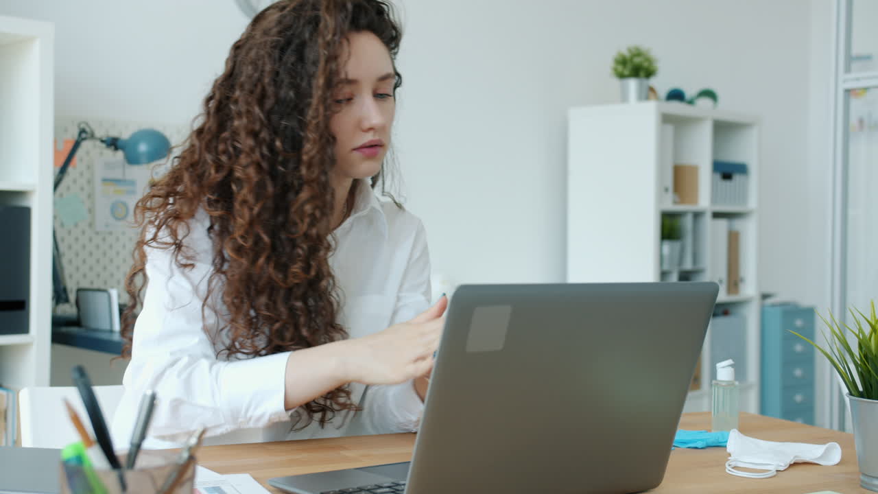 Woman Sanitizing Hands During Video Call in Office