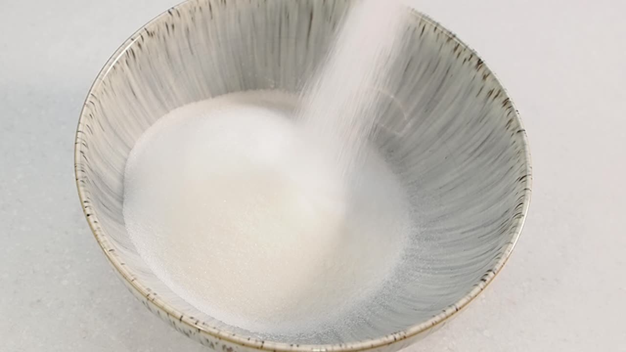 Zucchero bianco versato in una ciotola di ceramica grigia.