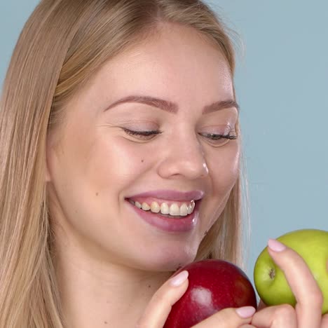 Close-up-studio-shot-of-smiling-young-woman-holding-two-apples--red-and-green