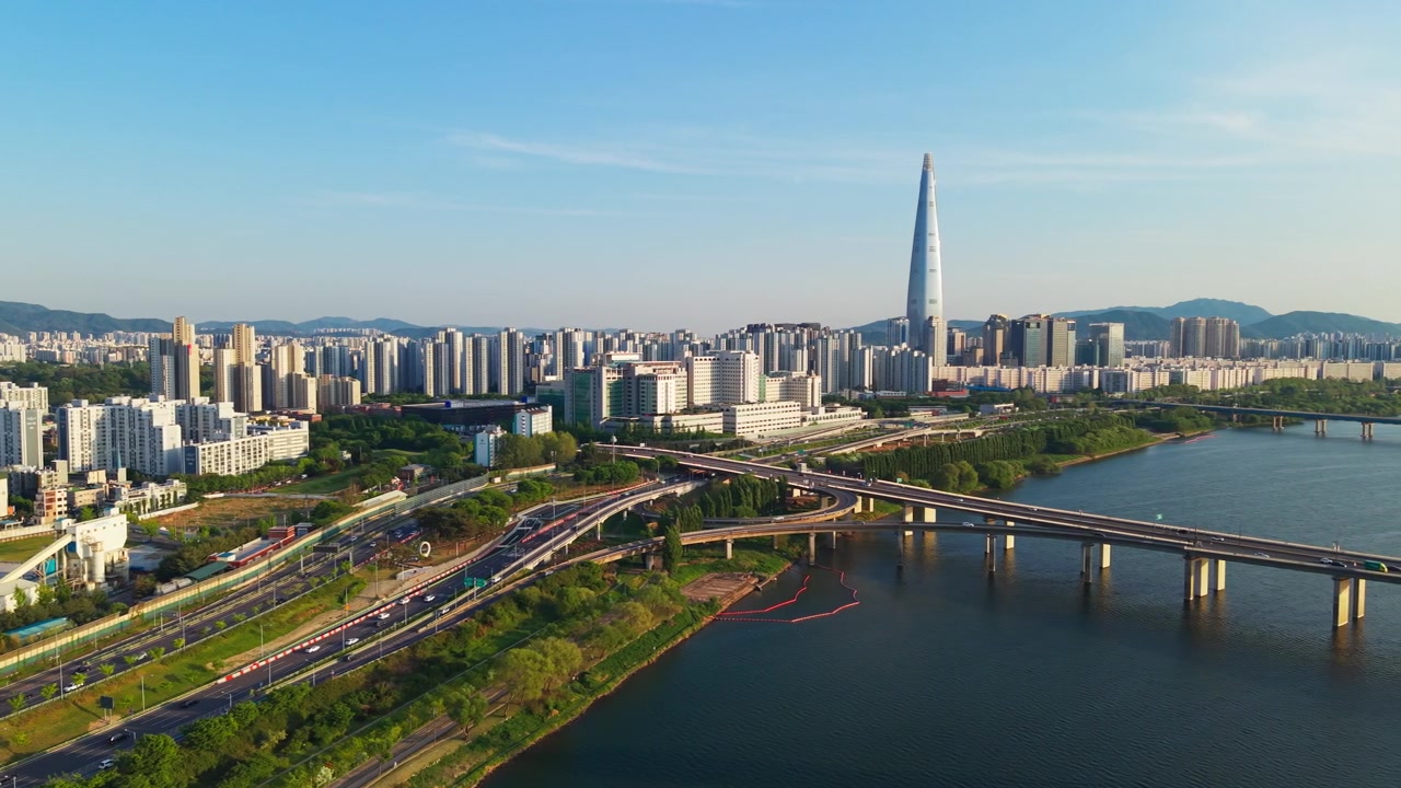 Vedute aeree panoramiche dell'iconico grattacielo Lotte World Tower che si erge sul fiume Han, traffico sulla superstrada Olympic-daero e sul ponte Olimpico sotto un cielo azzurro limpido a Seoul, Corea del Sud