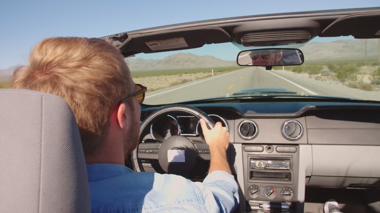 Uomo in auto decappottabile che guida lungo una strada aperta ripreso con R3D