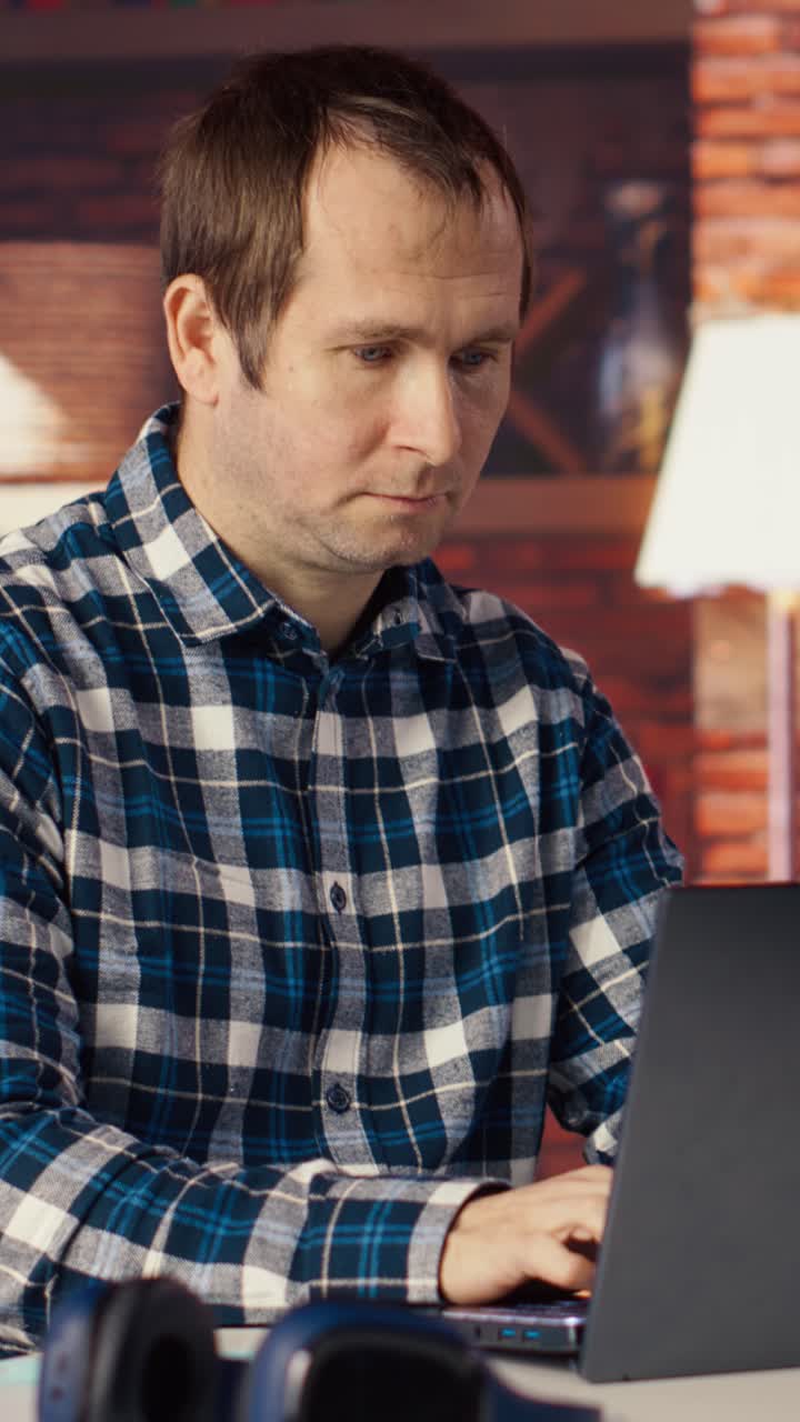 Vertical video Man seated at home office desk using laptop, checking emails