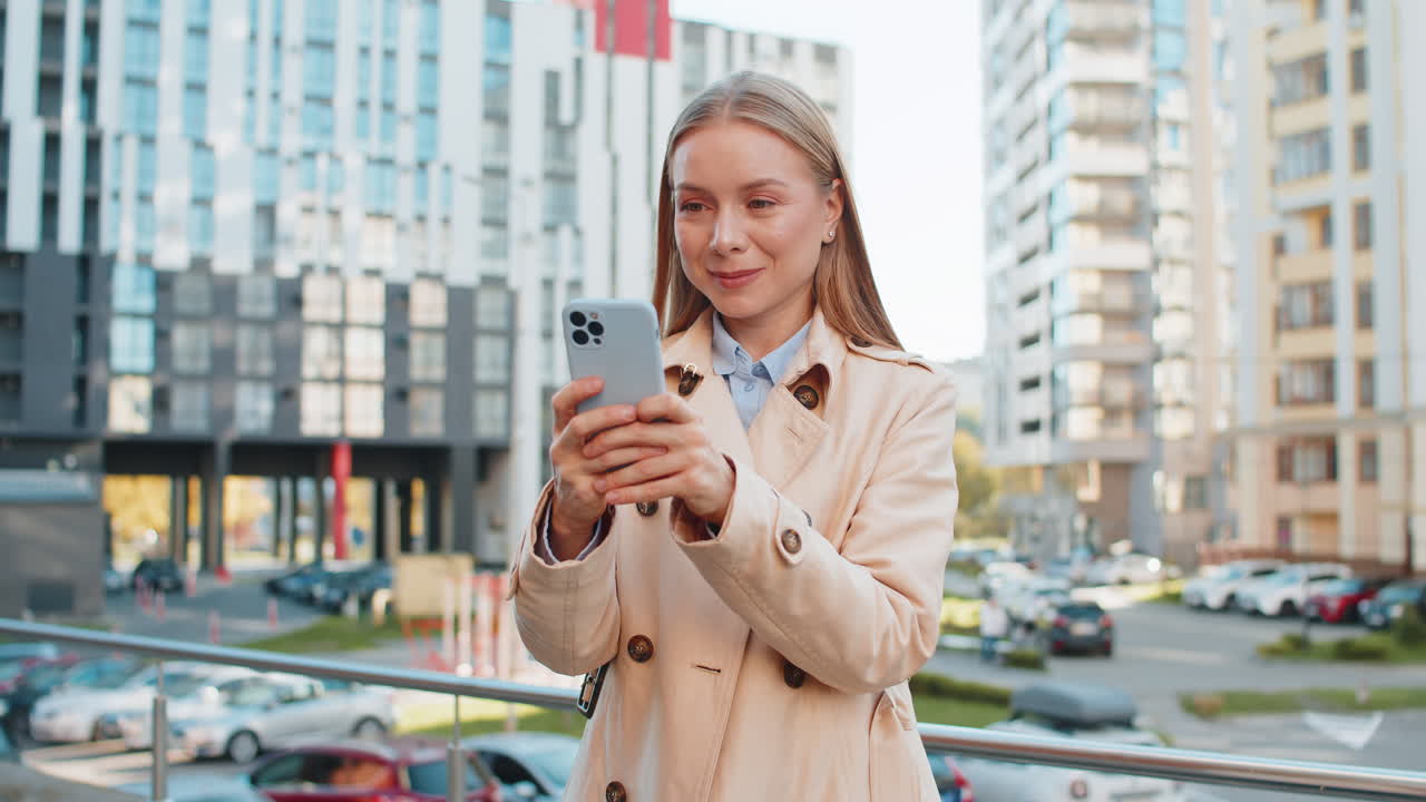 Una donna d'affari matura sorridente che chatta su Internet tramite telefono cellulare in piedi in una strada del centro della città