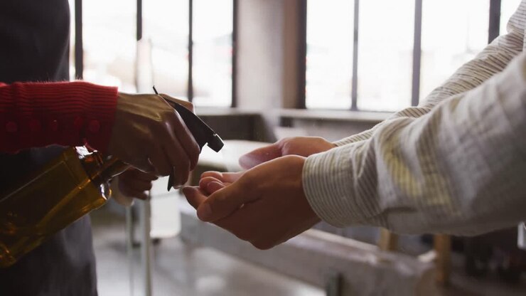 Midsection of woman at bar, holding thermometer, using sanitising spray on hands of male colleague