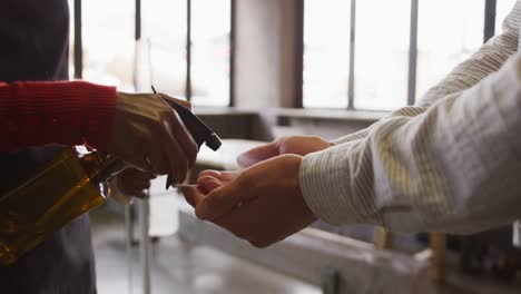 Midsection-of-woman-at-bar,-holding-thermometer,-using-sanitising-spray-on-hands-of-male-colleague