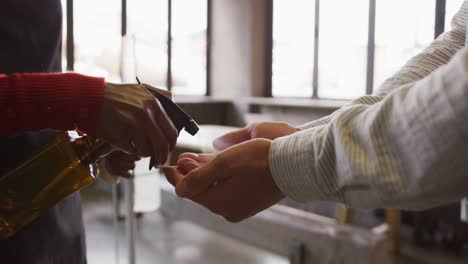 sección media de una mujer en una barra, sosteniendo un termómetro, usando spray desinfectante en las manos de un colega masculino
