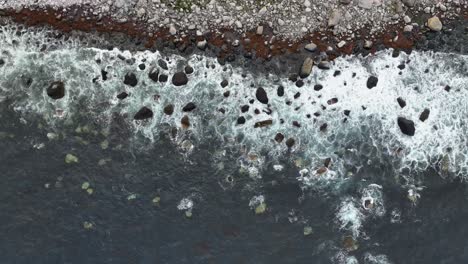 Icelandic-rocky-beach-top-down-aerial---Upward-moving-aerial-showing-ocean-waves-slowly-crushing-into-rocky-shoreline