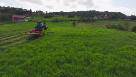 drone tracking shot of tractor with mower conditioner harvesting lush field crop