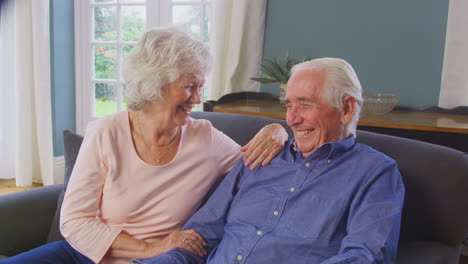 Una-Pareja-De-Ancianos-Amorosos-Disfrutando-De-Su-Jubilación-Sentados-En-Un-Sofá-En-Casa-Hablando-Y-Riendo-Juntos