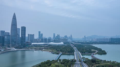 Panoramic-night-view-of-river-city-skyline-skyscraper-high-rise-building-landmark-near-mountain,-traffic-flow-over-bridge