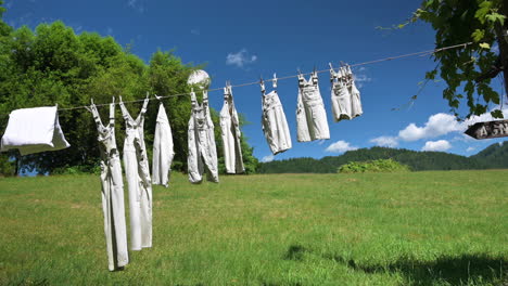 vintage clothing hanging outside against green field and blue sky with white clouds background on a sunny day - static shot