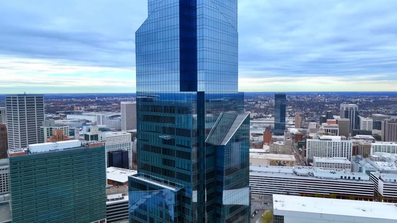 Skyline aereo del centro città con grattacielo di vetro, cielo coperto che proietta tonalità fredde, facciata riflettente a specchio