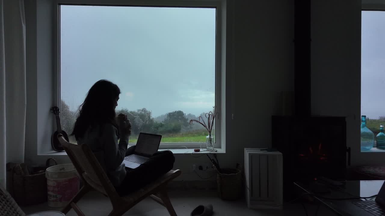 Slow motion woman teleworking on a laptop while sitting near a window and chimney