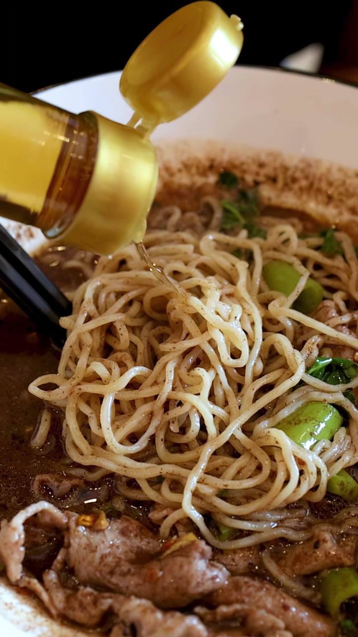 Primo piano di noodle tailandesi "boat noodles" conditi con salsa di pesce da una bottiglia sul brodo.