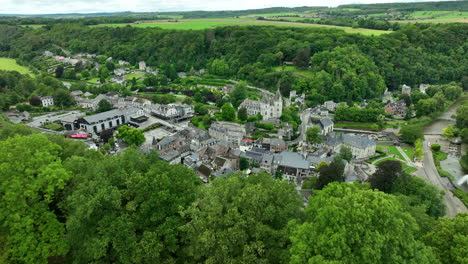 revelación aérea de la ciudad de durbuy desde detrás de la cima de una colina boscosa verde