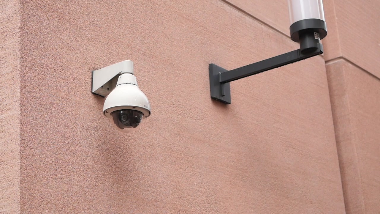 White Security Camera Mounted on Building Wall Next to Light