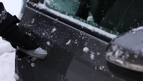 a person with gloves is opening the car door with fresh snow