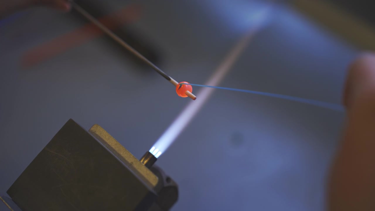 Close up of a glass artist shaping a glowing red bead with a blowtorch flame at a traditional jewelry workshop in Vikten, Lofoten Islands, Norway